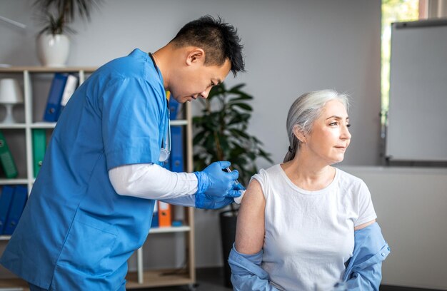 Un médecin asiatique adulte sérieux fait une injection à une vieille patiente à l'intérieur du bureau de la clinique