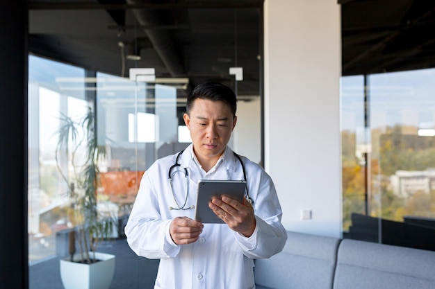 Un médecin asiatique sérieux utilise une tablette, l'homme travaille dans une clinique moderne