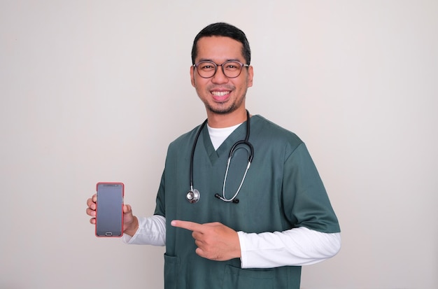 Photo médecin asiatique souriant et pointant vers l'écran vierge du téléphone portable qu'il tient