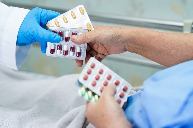 Médecin asiatique tenant des pilules de capsule d'antibiotiques dans un emballage blister avec un patient senior.