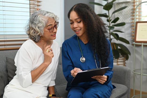 Un médecin attentif montrant une tablette numérique et expliquant le rapport médical à une femme âgée Le concept de service de soins de santé à domicile