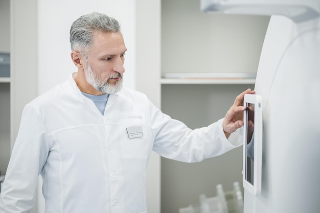 Médecin au travail Radiologue mature debout près de l'équipement médical et ayant l'air occupé