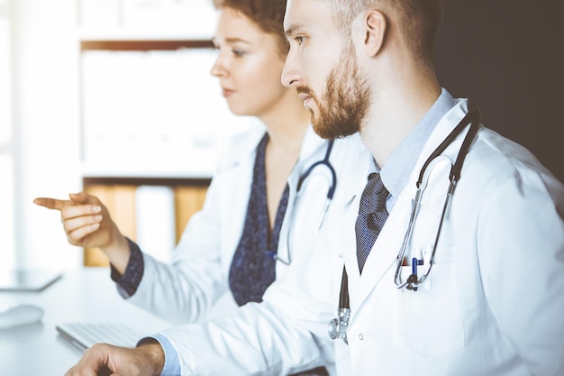 Médecin à barbe rouge avec une collègue discutant de la thérapie actuelle de la maladie tout en étant assis sur le lieu de travail dans une clinique ensoleillée. Travail d'équipe en médecine.