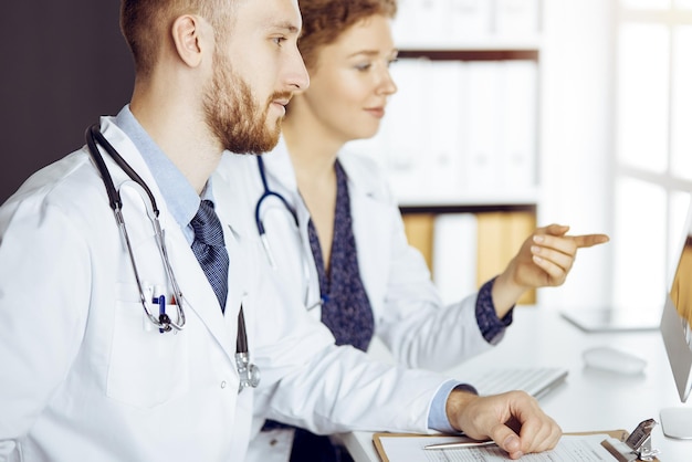 Médecin barbu avec une collègue discutant de la thérapie actuelle de la maladie alors qu'il était assis sur le lieu de travail dans une clinique ensoleillée. Travail d'équipe en médecine