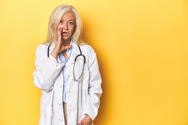 Une médecin blanche d'âge moyen sur une toile de fond jaune dit une nouvelle secrète.