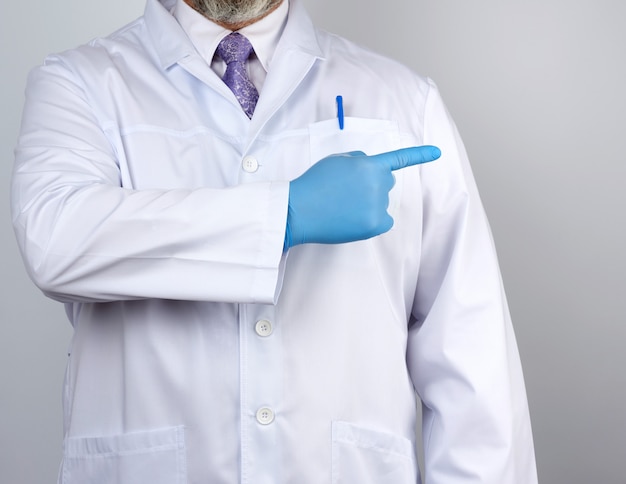 Médecin en blouse blanche avec des boutons, sur les mains avec des gants stériles bleus, montrant le geste de la main indiquant le sujet