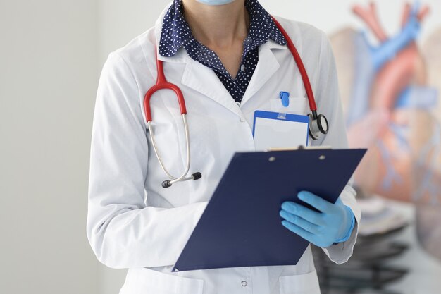 Médecin en blouse blanche et gants tient le presse-papiers.