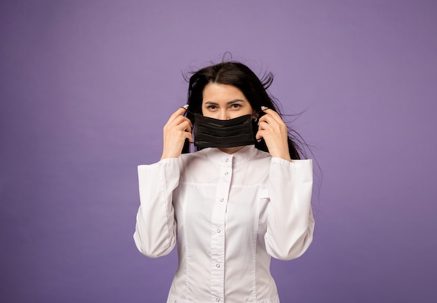 Médecin en blouse médicale porte un masque médical noir sur violet