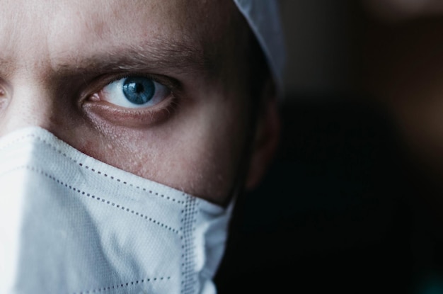 médecin chirurgien en uniforme blanc dans une salle d'opération sombre regarde la caméra