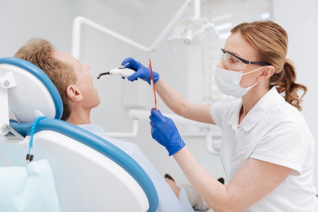 Médecin compétent et consciencieux qui blanchit les dents des patients en utilisant la technologie la plus contemporaine et en étant très précis