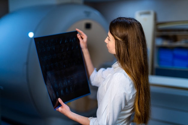 Photo médecin compétent lisant les rayons x près de l'appareil d'imagerie par résonance magnétique.