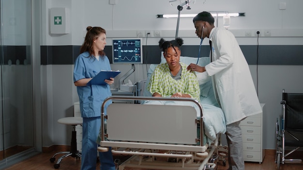 Médecin consultant une jeune femme avec un stéthoscope au lit pour mesurer le rythme cardiaque et la pression du pouls. Homme travaillant comme médecin faisant un examen médical pendant qu'une infirmière donne de l'aide.