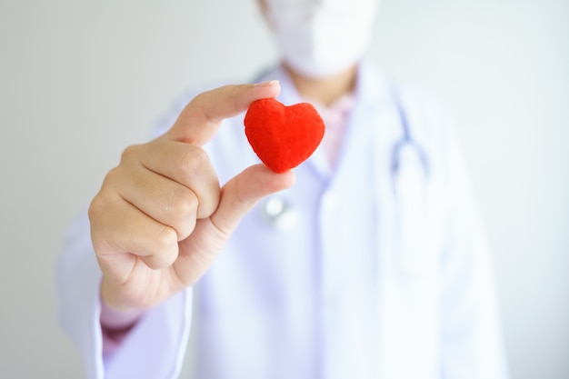 Médecin de contrôle cardiaque tenant un coeur rouge sur les mains au bureau de l'hôpital. Concept de soins de santé et médical.