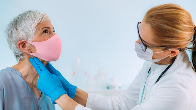 Photo médecin de contrôle de la glande thyroïde examinant une femme âgée à la clinique