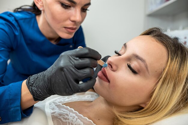 Photo le médecin cosmétologue applique de la cire dépilatoire sur les lèvres d'une jeune cliente pour enlever les poils indésirables