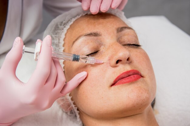 Le médecin cosmétologue effectue la procédure d'injections faciales. Jeune femme dans un salon de beauté.