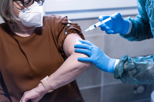 Médecin en costume de matières dangereuses donnant au patient un vaccin contre la maladie à coronavirus Femme âgée portant un masque protecteur faisant le vaccin contre la maladie de Covid19 Concept médical et de soins de santé Se concentrer sur les gants