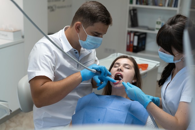 Médecin dentiste masculin et infirmière traitant les dents d'une femme assise sur une chaise. Les orthodontistes pratiquent des prothèses. Espace de copie. Concept de médecine et de cavité buccale.