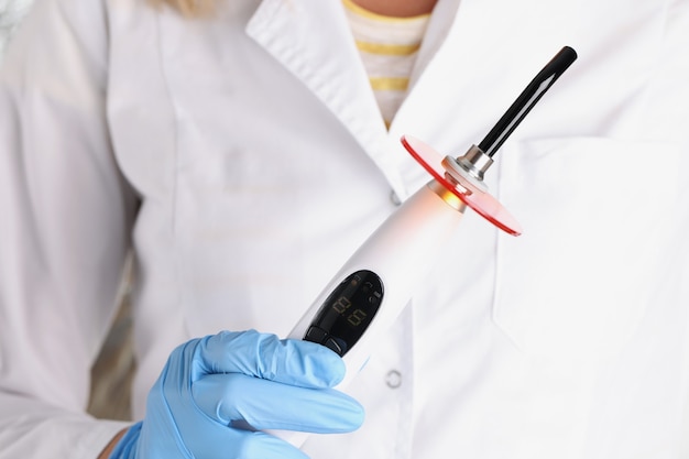 Médecin dentiste tenant une machine légère pour le traitement des caries en gros plan