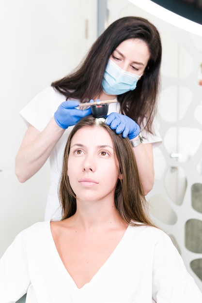 Photo le médecin dermatologue examinant les cheveux et le cuir chevelu des femmes avec un appareil spécial pour le diagnostic