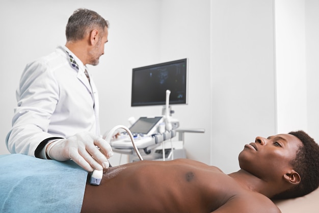 Médecin diagnostiquant le ventre d'un homme avec une sonde à ultrasons.