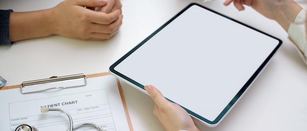 Médecin diagnostiquer le patient avec une tablette écran vierge, un dossier patient et un stéthoscope dans la salle d'examen