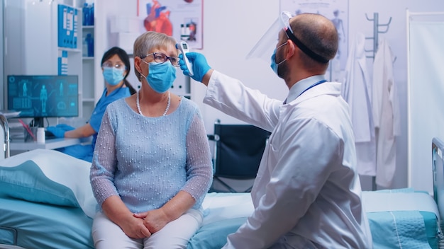 Le médecin dicte les informations du patient à l'infirmière et elle les écrit sur le PC. Vieille femme âgée à la retraite portant un masque et un travailleur de la santé dans un équipement de protection pour consultation.
