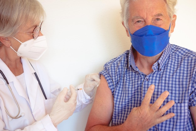 Médecin donnant une injection à un homme caucasien âgé âgé à la retraite recevant un rappel de vaccin covid 19 personnes portant un masque