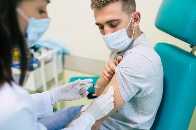 Médecin du vaccin Covid-19 ou coronavirus tenant une seringue et utilisant du coton avant de faire l'injection au patient dans le masque médical.