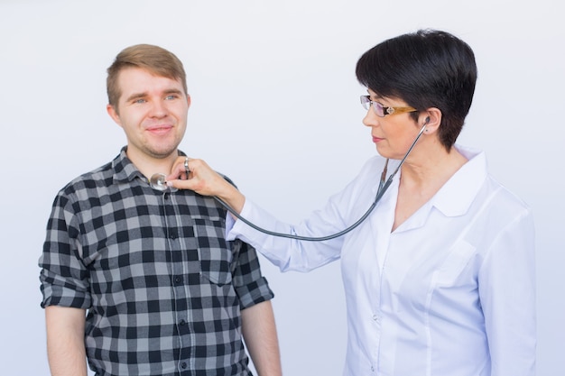 Médecin à l'écoute de la poitrine des patients avec stéthoscope sur fond blanc.