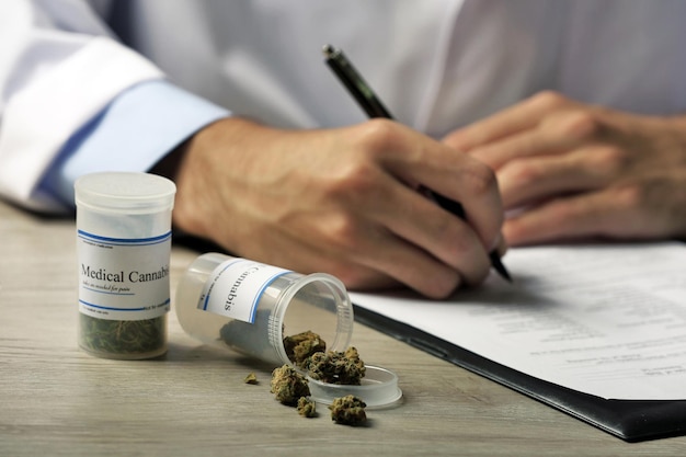 Médecin écrivant sur ordonnance vierge et bouteille de cannabis médical sur table en gros plan