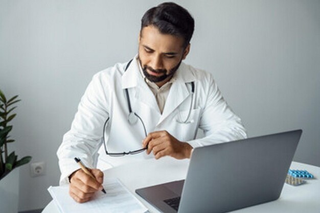 un médecin est assis à un bureau avec un ordinateur portable et un stylo devant lui