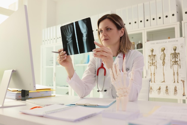 Médecin étudie la photo radiographique du bras du patient assis au bureau