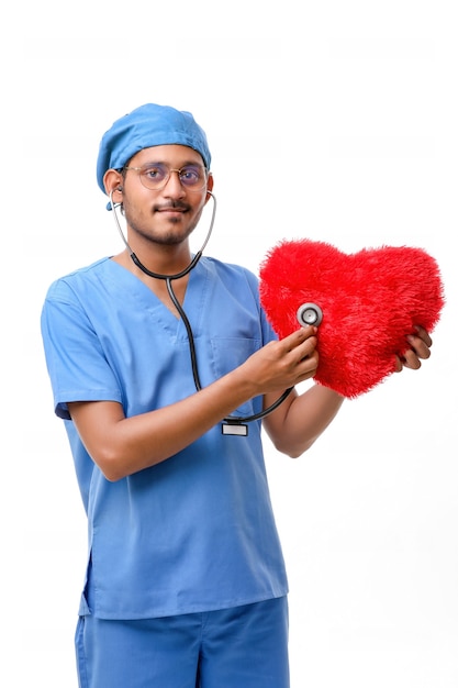 Médecin examinant un oreiller en forme de coeur rouge avec un stéthoscope sur fond blanc.