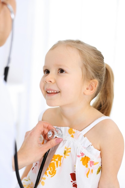 Médecin examinant une petite fille au stéthoscope. Heureux enfant patient souriant à l'inspection médicale habituelle. Concepts de médecine et de soins de santé.