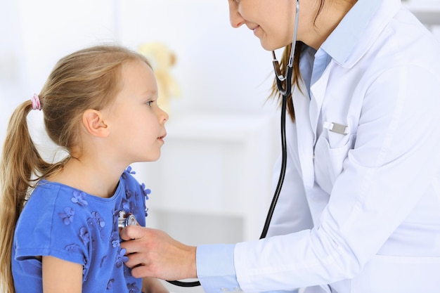 Médecin examinant une petite fille au stéthoscope. Heureux enfant patient souriant à l'inspection médicale habituelle. Concepts de médecine et de soins de santé.