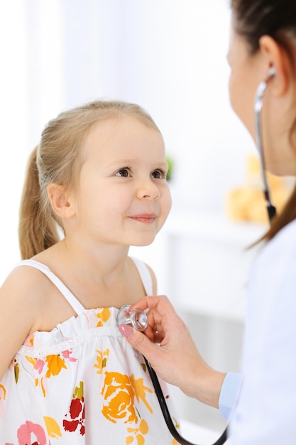 Médecin examinant une petite fille au stéthoscope. Heureux enfant patient souriant à l'inspection médicale habituelle. Concepts de médecine et de soins de santé.