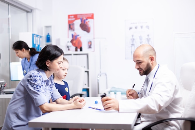 Médecin expliquant le traitement à la mère de l'enfant malade dans le bureau de l'hôpital tenant une bouteille de pilules. Médecin de santé spécialiste en médecine fournissant un examen de traitement des services de santé.