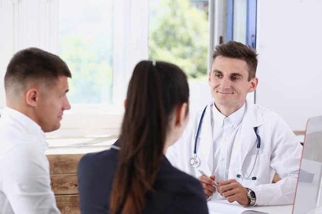 Médecin de famille masculin écouter attentivement jeune couple en portrait de bureau.