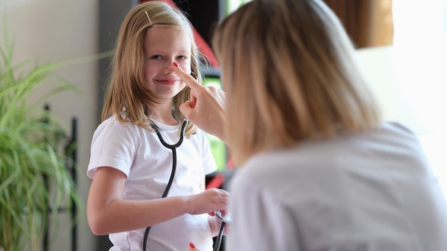 Le médecin de famille touche le nez d'une écolière tenant un stéthoscope Le pédiatre joue avec son jeune