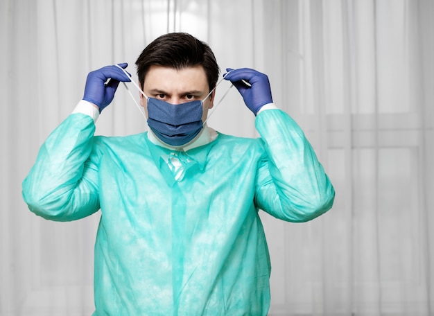 Un médecin fatigué en équipement de protection à la maison met un masque médical de protection, une épidémie de coronavirus