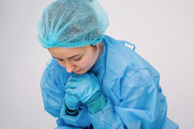 Médecin fatigué en uniforme médical prie en regardant l'aide sur fond gris isolé