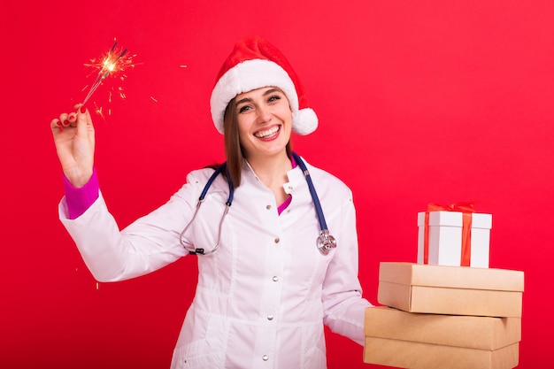 Le médecin félicite les patients de la clinique pour Noël et le Nouvel An Jeune femme avec des coffrets cadeaux et des cierges magiques sur fond rouge