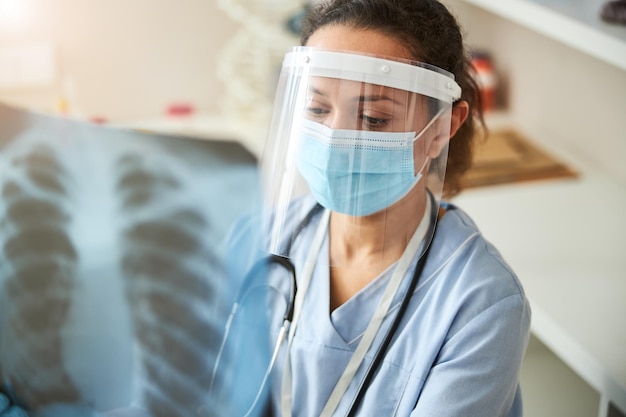 Photo médecin féminin sérieux examinant une radiographie pulmonaire