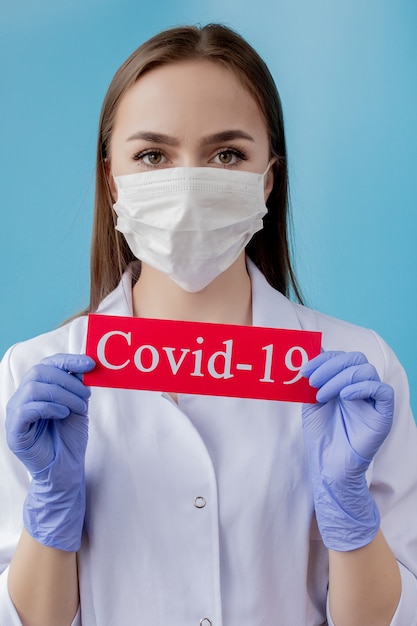 Médecin femme avec masque chirurgical pointant sur du papier rouge avec Coronavirus mesaage sur fond bleu. Organisation mondiale de la santé L'OMS a introduit un nouveau nom officiel pour la maladie à coronavirus nommé COVID-19