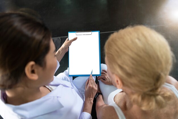 Médecin Avec Femme Senior En Centre De Réadaptation. Entraîneur Personnel Montrant Quelque Chose Sur Le Presse-papiers.