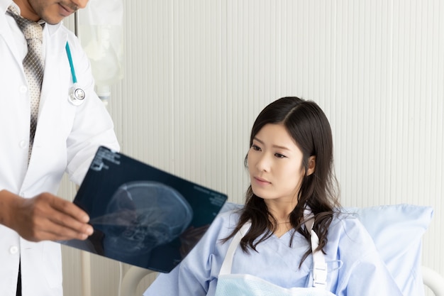 Photo médecin avec film radiographique et patiente asiatique sur un lit à l'hôpital
