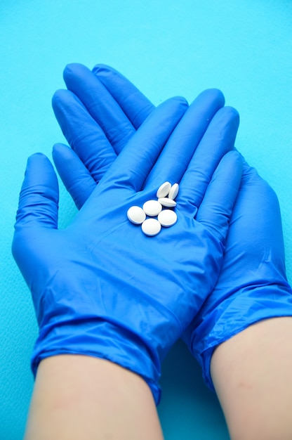 Un médecin en gants médicaux détient des pilules blanches Fond bleu