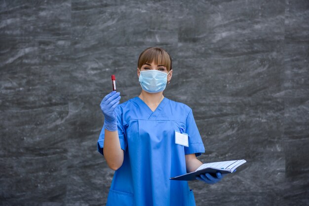 Médecin en gants de protection et masque tenant un tube à essai rouge