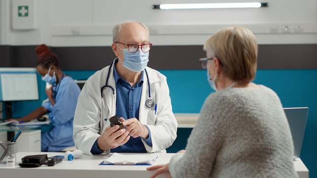 Médecin généraliste donnant une bouteille de pilules comme traitement de la maladie à une femme retraitée malade lors d'un rendez-vous pendant la pandémie de covid 19. Médicament sur ordonnance avec flacon d'analgésiques et de médicaments.